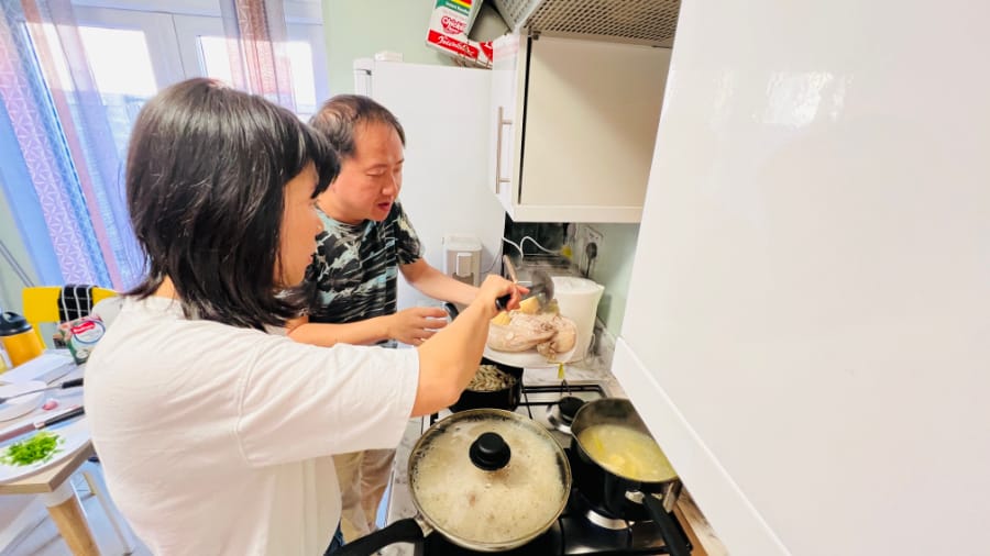 与友人努力重现熟悉的鸡饭味道 (一男一女一起准备白斩鸡，锅里还在煮鸡汤和鸡油饭)