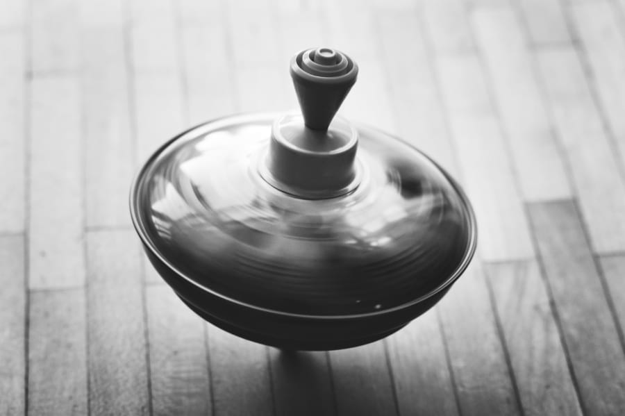 旋转的陀螺 旋转的陀螺 (高角度黑白照片,聚焦于一只正在旋转的陀螺,陀螺表面带有动感模糊,底部为浅色木地板。)