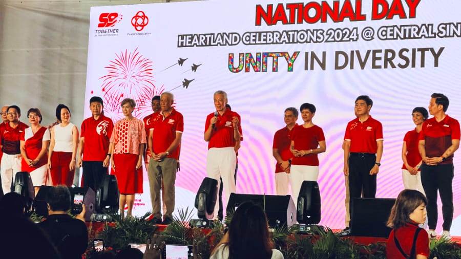 某年碧山国庆庆祝会看到的议员和部长群 (一群约15人在舞台上穿红白服装，背后大屏幕显示&ldquo;National Day&rdquo;和&ldquo;Unity in Diversity&rdquo;等字样，台下有观众观看)