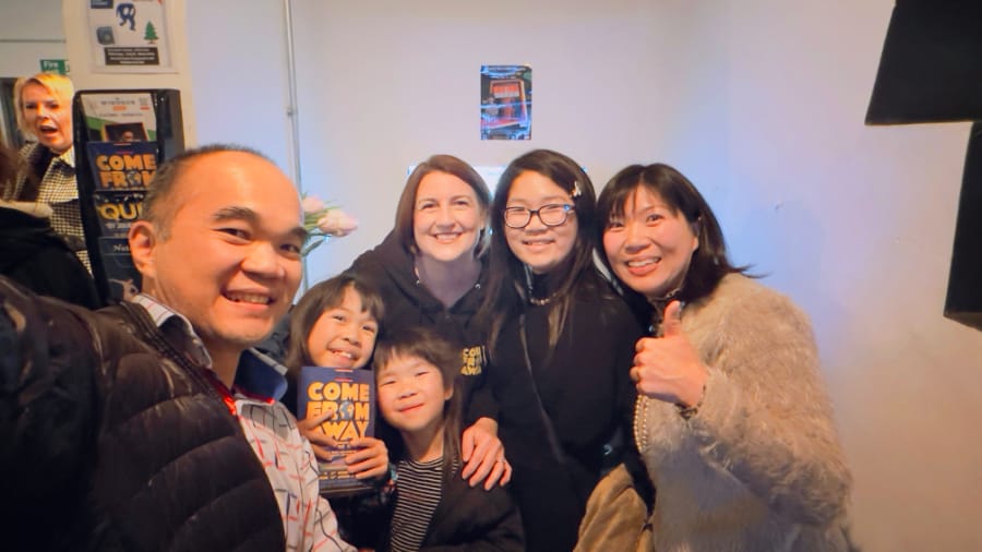 我们一家去支持SARAH的公演 (多人围成一排微笑，有人竖大拇指，画面中可见《COME FROM AWAY》节目册封面)